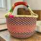 Medium round Bolga basket with a navy, orange, magenta and green checkerboard weave, leather handles