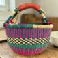 Medium round Bolga basket with a teal and magenta checker weave with a cream-and-black band, leather handles