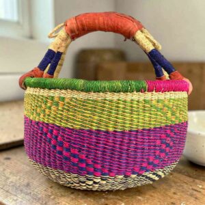 Medium round Bolga basket with a natural top band flecked green and orange, with a magenta and navy diamond pattern below, leather handles