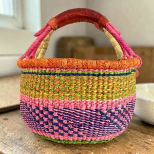 Medium round Bolga basket with an orange rim and fleck band with a pink-and-navy diamond pattern below, leather handles