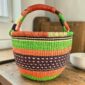 Medium round Bolga basket with an orange-and-cream rim with green, orange and plum bands, the plum band with cream dot detail, leather handles