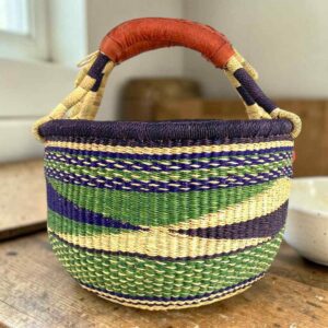 Medium round Bolga basket with a dark purple rim with a green, navy and cream diagonal wave pattern, leather handles
