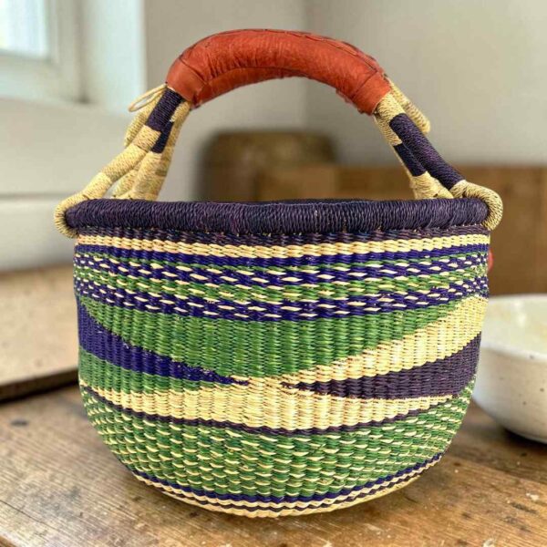 medium-round-basket-683-sunbird-bolga-main Medium round Bolga basket with a dark purple rim with a green, navy and cream diagonal wave pattern, leather handles
