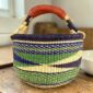 Medium round Bolga basket with a dark purple rim with a green, navy and cream diagonal wave pattern, leather handles