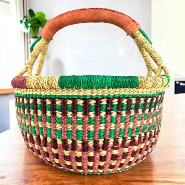 Rich-toned checked medium round Bolga basket with leather-wrapped handle, on a timber table