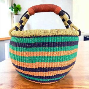 Cool and warm striped medium round Bolga basket with leather-wrapped handle, on a timber table