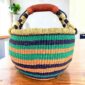 Cool and warm striped medium round Bolga basket with leather-wrapped handle, on a timber table