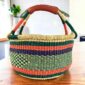 Deep-toned striped medium round Bolga basket with leather-wrapped handle, on a timber table