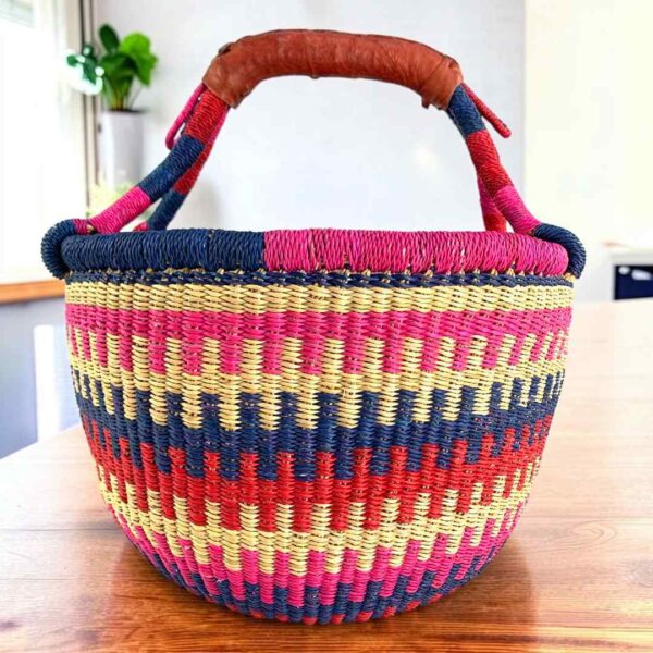 medium-round-basket-694-lucky-bright-stepped-stripe-bolga-woven-bashiri-main Bright stepped-stripe medium round Bolga basket with leather-wrapped handle, on a timber table