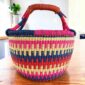 Bright stepped-stripe medium round Bolga basket with leather-wrapped handle, on a timber table