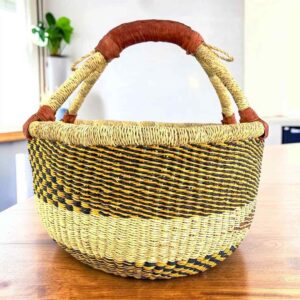 Neutral-toned medium round Bolga basket with a dark diagonal pattern with leather-wrapped handle, on a timber table