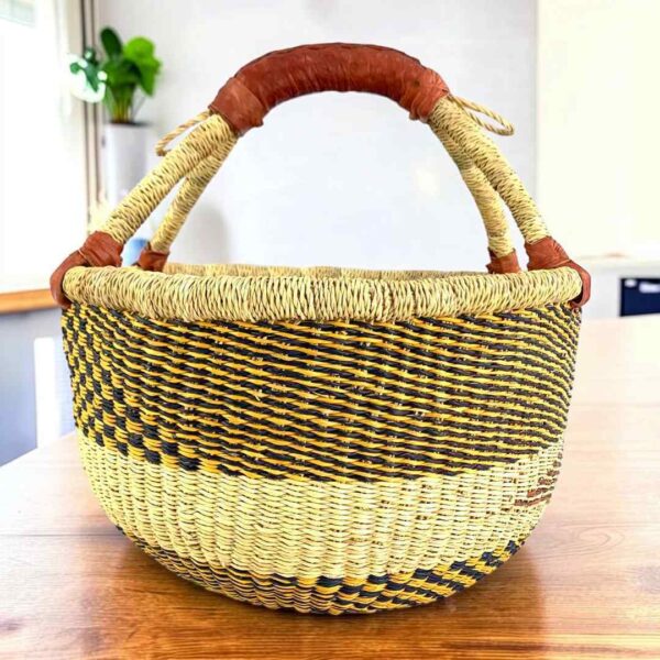 Neutral-toned medium round Bolga basket with a dark diagonal pattern with leather-wrapped handle, on a timber table