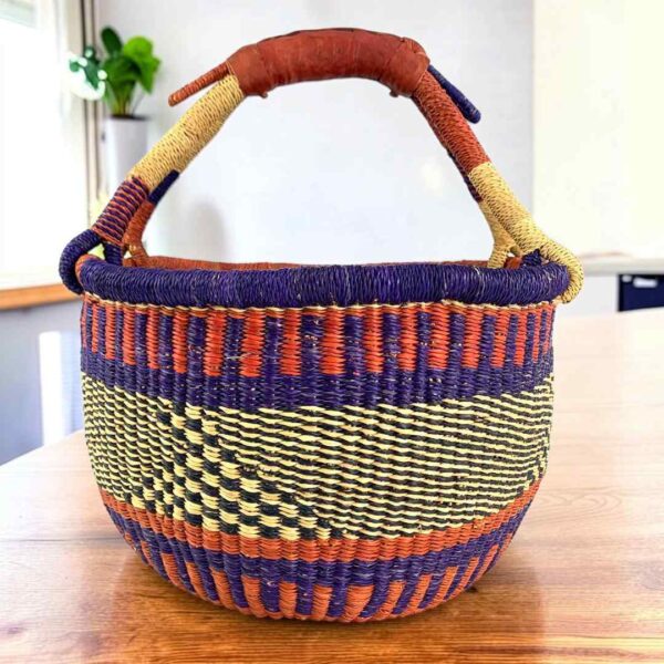 Deep warm-toned checked medium round Bolga basket with leather-wrapped handle, on a timber table