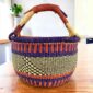 Deep warm-toned checked medium round Bolga basket with leather-wrapped handle, on a timber table