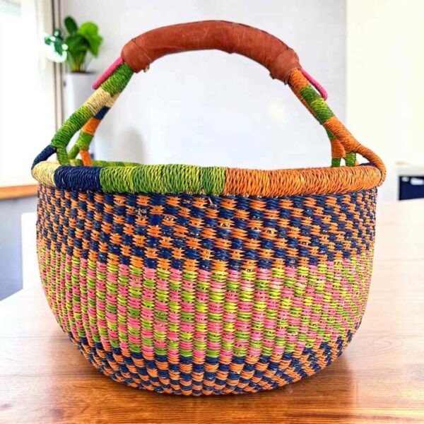 Multi-tone checked medium round Bolga basket with leather-wrapped handle, on a timber table