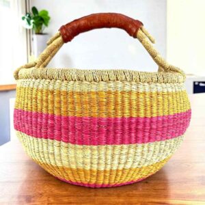 Warm pastel banded medium round Bolga basket with leather-wrapped handle, on a timber table