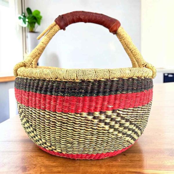 medium-round-basket-699-warmday-warm-dark-banded-bolga-african-basket-bashiri-main Warm and dark banded medium round Bolga basket with leather-wrapped handle, on a timber table
