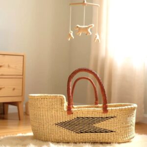 Handwoven Moses baby carry basket with star pattern and leather handles, placed on a sheepskin rug in a softly lit nursery.