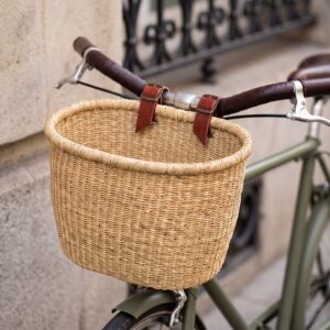 a bicycle basket in natural colour attached to a bike by leather straps.