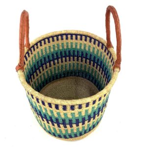 Angled view of the open laundry basket with navy, teal and green bands on natural straw and tall leather handles