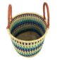 Angled view of the open laundry basket with navy, teal and green bands on natural straw and tall leather handles