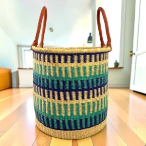 Open laundry basket with navy, teal and green bands on natural straw and tall leather handles