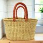 Oval Bolga basket with natural undyed straw and leather handles, on a wooden kitchen bench