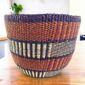 Vegan planter basket in earthy tones with bands of vertical stripes, on a timber table