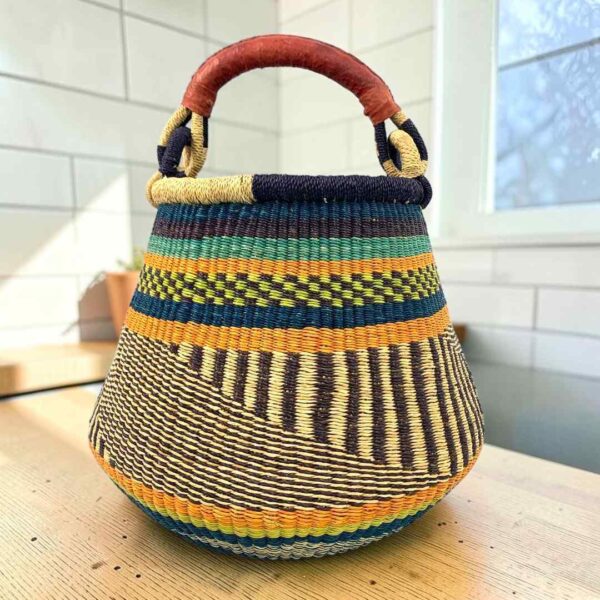 Bolga pot basket with orange, navy and green bands above a black and natural diagonal pattern and a leather-wrapped handle