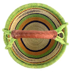 Top-down view inside the large round Bolga basket with bright leafy and citrus bands and deep inky stripes, showing the coiled base and leather handle