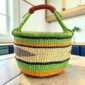 Large round Bolga basket with bright leafy and citrus bands and deep inky stripes, leather-wrapped handle, on a timber benchtop