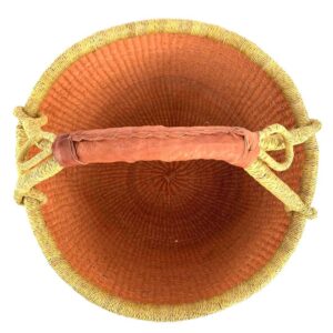Top-down view inside the large round Bolga basket with a single warm terracotta tone and natural rim, showing the coiled base and leather handle