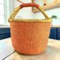 Large round Bolga basket with a single warm terracotta tone and natural rim, leather-wrapped handle, on a timber benchtop