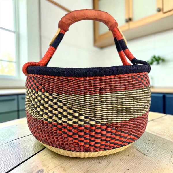 Large round Bolga basket with deep red and inky diagonal sections, leather-wrapped handle, on a timber benchtop