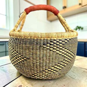 Large round Bolga basket with natural straw and deep inky fine checks, leather-wrapped handle, on a timber benchtop