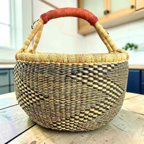 Large round Bolga basket with natural straw and deep inky fine checks, leather-wrapped handle, on a timber benchtop