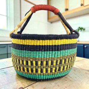 Large round Bolga basket with bold sunny, sea-green and deep inky bands, leather-wrapped handle, on a timber benchtop