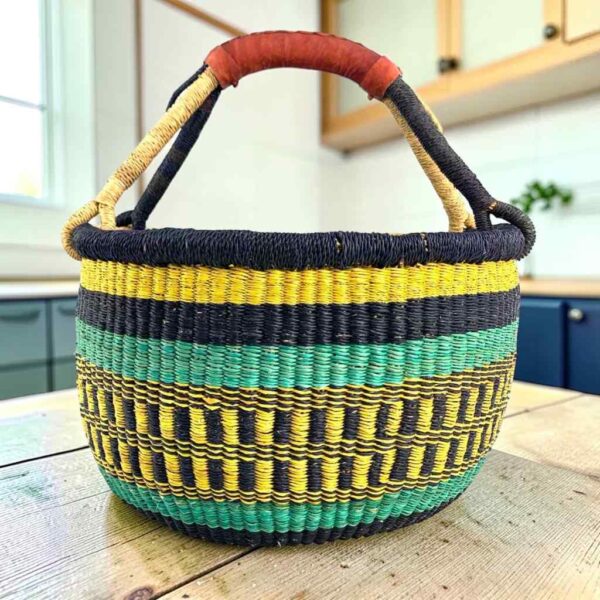 round-large-basket-861-serenity-navy-yellow-teal-bolga-woven-bashiri-main Large round Bolga basket with bold sunny, sea-green and deep inky bands, leather-wrapped handle, on a timber benchtop