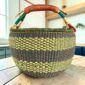 Large round Bolga basket with muted olive and slate tones with natural checks, leather-wrapped handle, on a timber benchtop