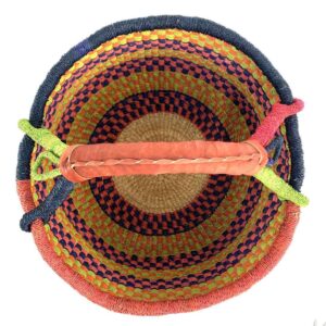 Top-down view inside the large round Bolga basket with bright citrus and rosy bands with deep inky checks, showing the coiled base and leather handle