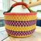 Large round Bolga basket with bright citrus and rosy bands with deep inky checks, leather-wrapped handle, on a timber benchtop