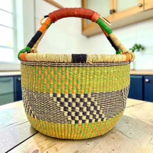 Large round Bolga basket with zesty citrus tones and a diagonal inky checked section, leather-wrapped handle, on a timber benchtop