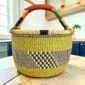 Large round Bolga basket with zesty citrus tones and a diagonal inky checked section, leather-wrapped handle, on a timber benchtop