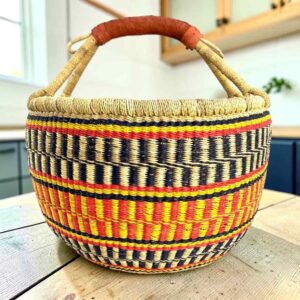 Large round Bolga basket with sunny and fiery bands with dark zigzag rows, leather-wrapped handle, on a timber benchtop