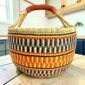 Large round Bolga basket with sunny and fiery bands with dark zigzag rows, leather-wrapped handle, on a timber benchtop