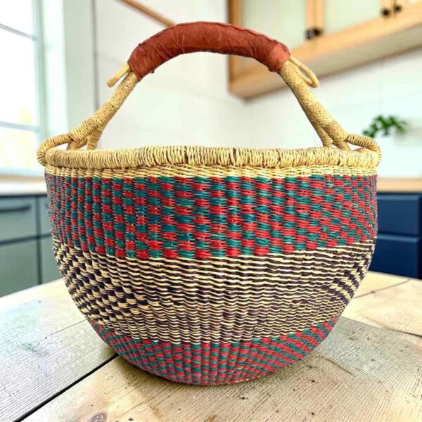 Large round Bolga basket with a sea-green and berry band over fine inky patterning, leather-wrapped handle, on a timber benchtop