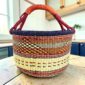 Large round Bolga basket with an inky rim over rust and amber patterning, leather-wrapped handle, on a timber benchtop