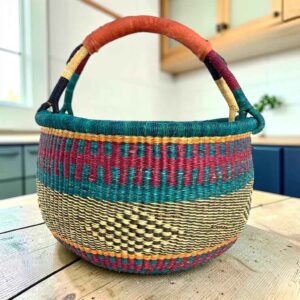 Large round Bolga basket with deep sea-green bands and berry stripes, leather-wrapped handle, on a timber benchtop