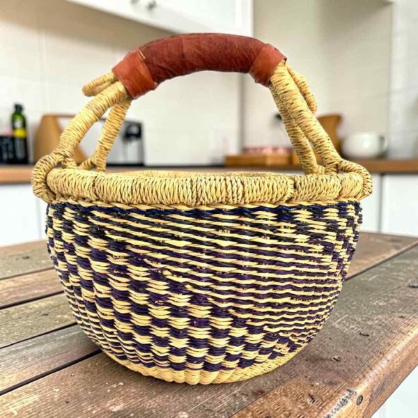 Small round Bolga basket with a navy and natural staggered check and a leather-wrapped handle, on a wooden table