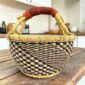 Small round Bolga basket with a navy and natural staggered check and a leather-wrapped handle, on a wooden table